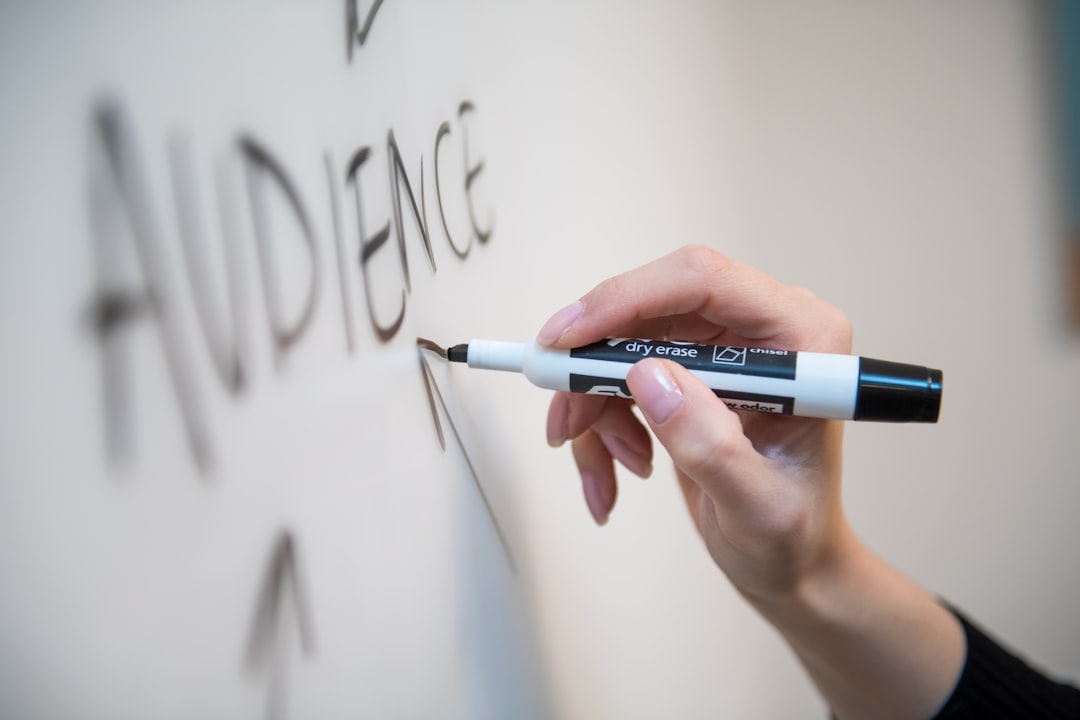A woman’s hand writing the word audience on a whiteboard, with arrows.